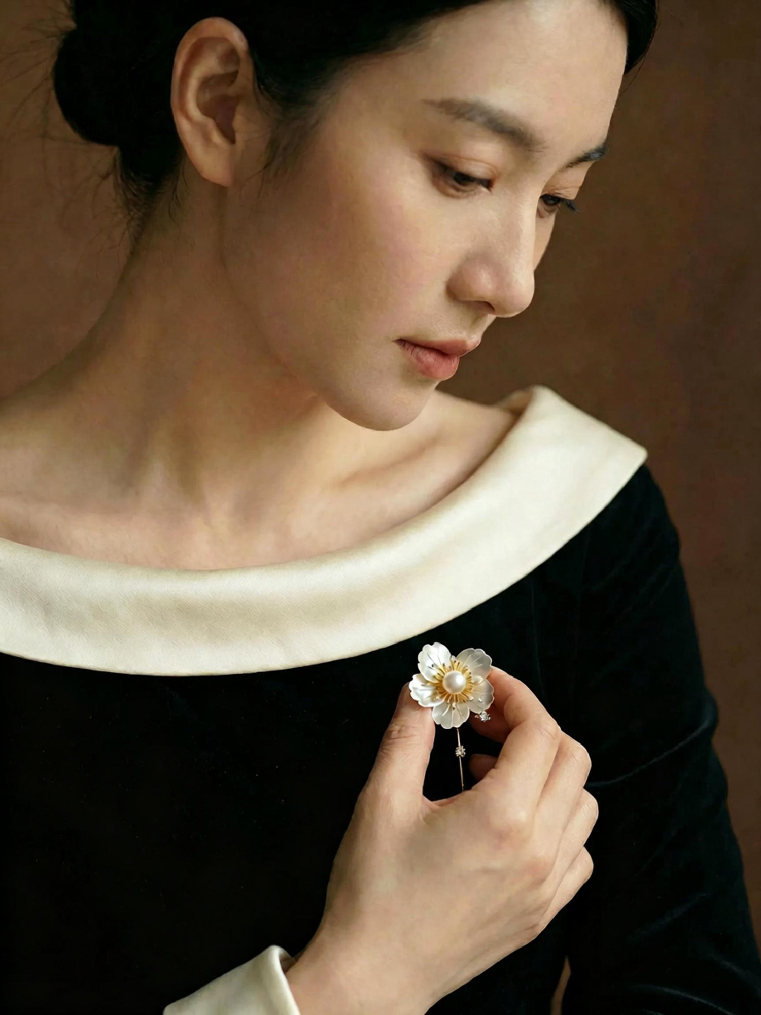 Camellia pearl brooch resting on warm beige stone, soft pearlescent luxury accessory