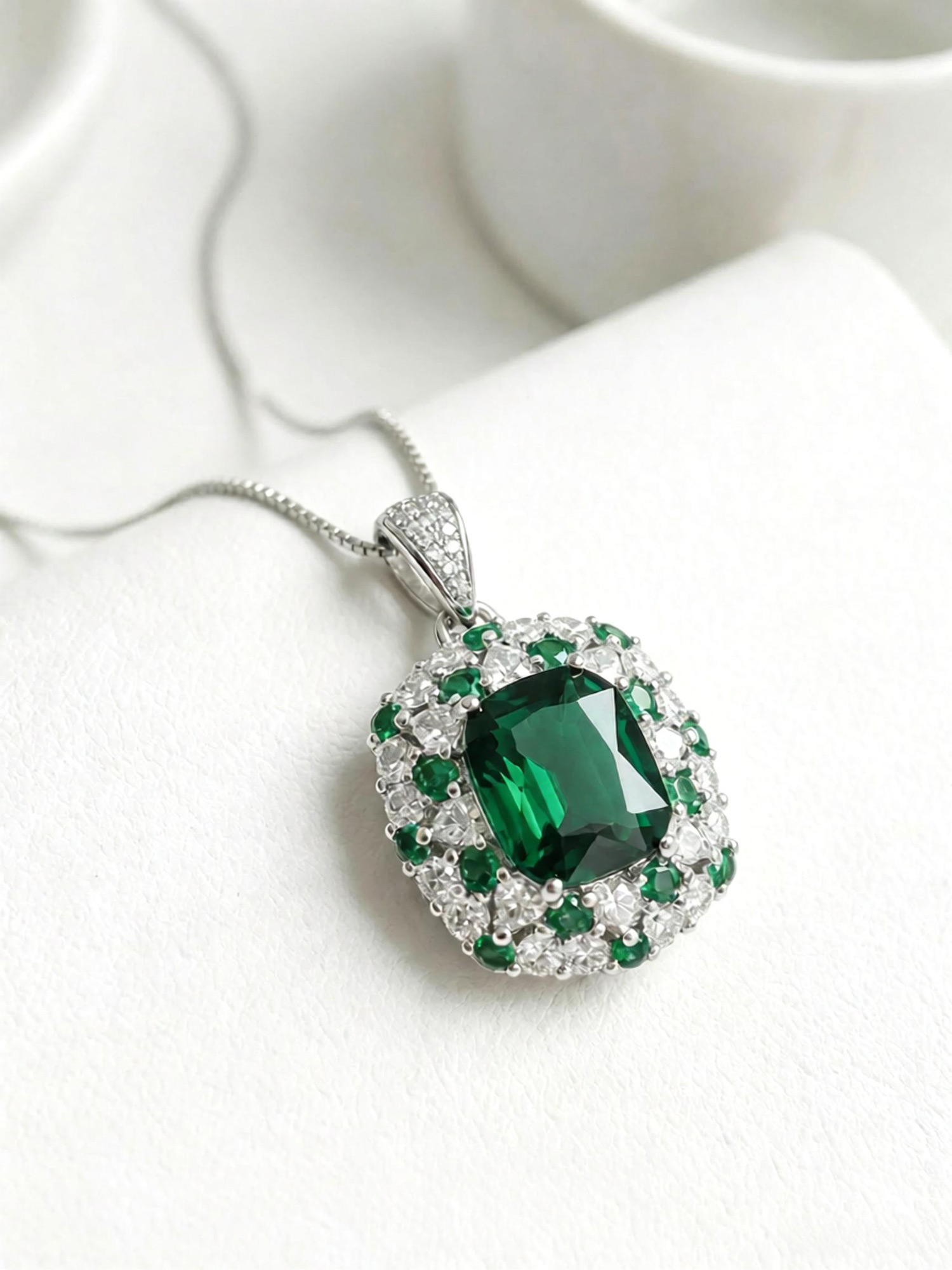 Emerald journey pendant necklace detail, layered zircon halo and emerald prong setting